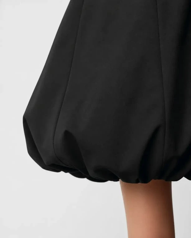Détail d’une robe ballon noire avec ourlet arrondi et tissu structuré